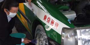 タクシーの前輪を洗剤を泡立て洗っている車両清掃注の写真